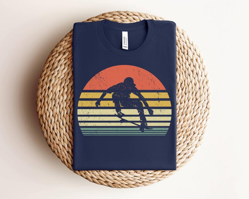 May include: A navy blue t-shirt with a vintage-style graphic of a person skateboarding in front of a sunset. The graphic has a faded, retro look with orange, yellow, and red colors.