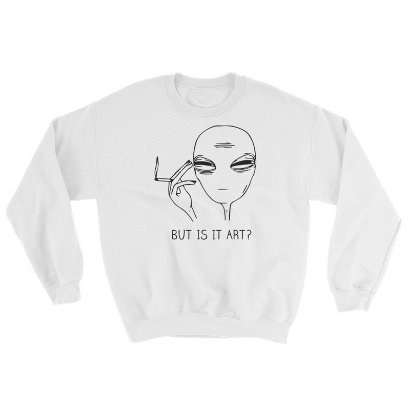 May include: White sweatshirt featuring a black and white illustration of an alien smoking a cigarette. The text "BUT IS IT ART?" is printed below the alien.