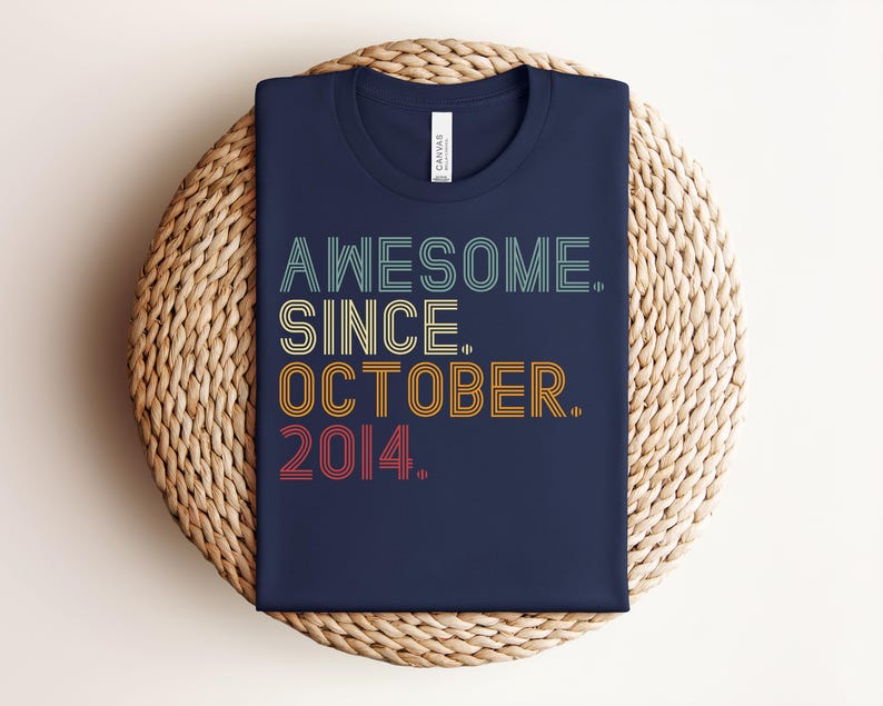 Puede incluir: Una camiseta azul marino de cuello redondo con el texto AWESOME. SINCE. OCTOBER. 2014. impreso en una fuente de estilo retro de varias l&iacute;neas. Las palabras est&aacute;n coloreadas en franjas horizontales de azul claro, amarillo, naranja y rojo.