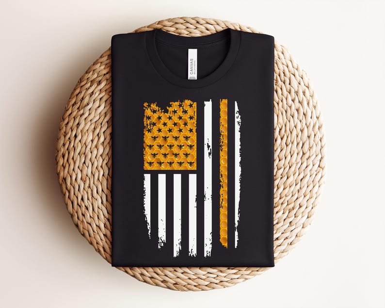 May include: A black crew neck t-shirt featuring a graphic of a stylised American flag. The flag's canton is filled with a yellow honeycomb pattern containing small black bee silhouettes, while the stripes are a mix of white and yellow honeycomb.