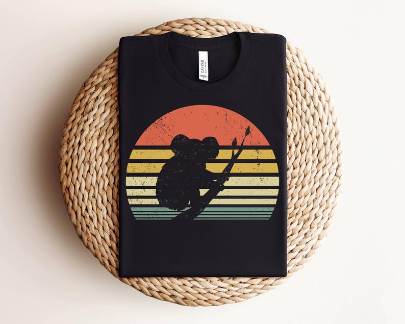 May include: Black t-shirt with a vintage-style graphic of a koala sitting on a branch in front of a sunset. The graphic has a retro color palette with shades of orange, yellow, and blue.
