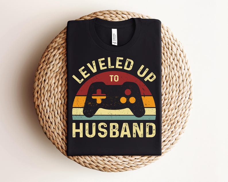 May include: Black t-shirt featuring a retro-style graphic that reads "Leveled Up To Husband" with a video game controller in the centre.