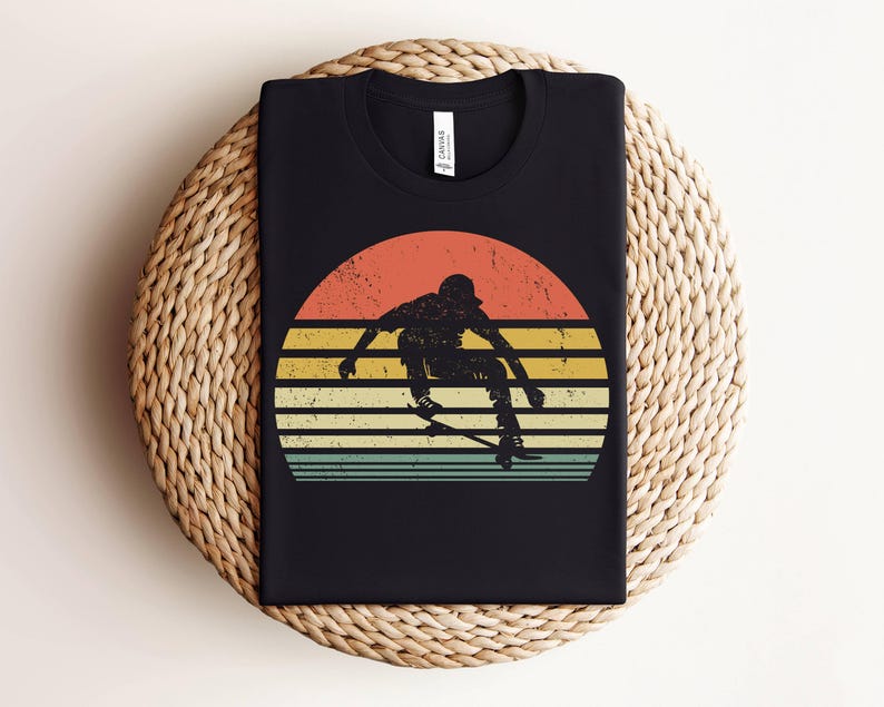 May include: A black t-shirt with a retro-style graphic of a person skateboarding in front of a sunset. The graphic has a faded, vintage look with a yellow, orange, and red sunset.