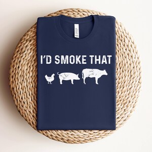 K&ouml;nnte beinhalten: Ein marineblaues T-Shirt mit dem Text "I'd Smoke That" in Wei&szlig;. Das Shirt zeigt eine wei&szlig;e Silhouette eines Huhns, eines Schweins und einer Kuh.