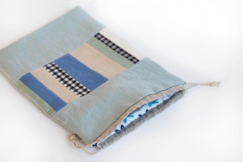 May include: A light blue drawstring bag made of patchwork fabric with a checkered pattern. The bag is folded and the drawstring is visible.