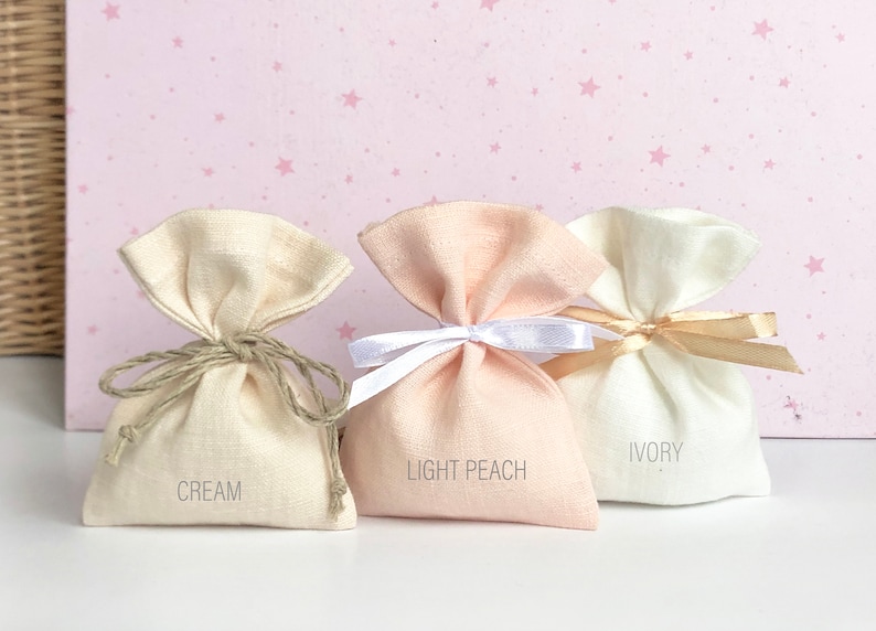 May include: Three small fabric gift bags in cream, light peach, and ivory colours. The bags are tied with different coloured ribbons and have the colour names printed on the front.
