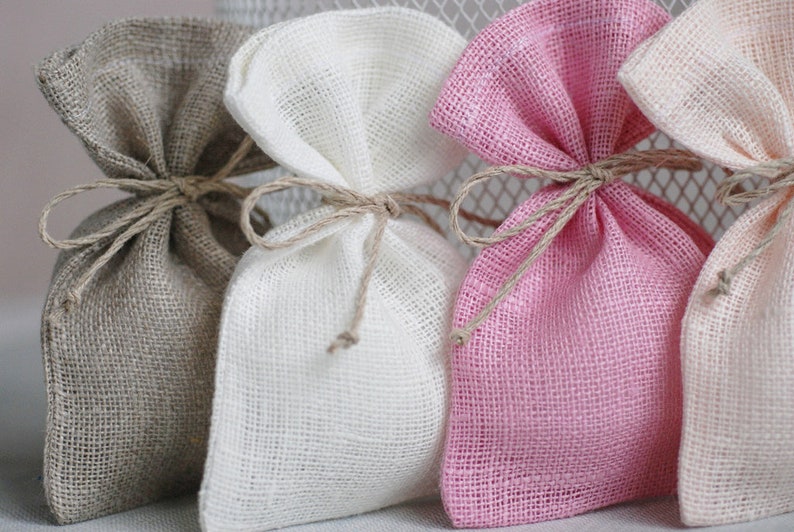 May include: Three small burlap gift bags tied with twine. The bags are beige, white, and pink.