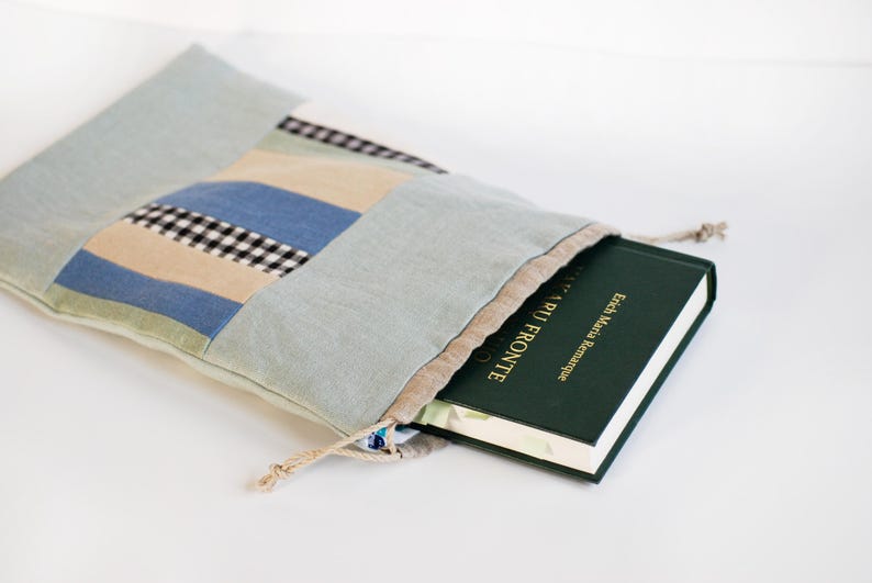 May include: A blue and white patchwork fabric drawstring bag with a book titled "Erich Maria Remarque All Quiet on the Western Front" inside.