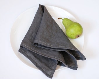 May include: A gray linen napkin folded on a white plate with a green pear beside it.