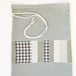 Può includere: Una borsa a cordoncino di colore verde chiaro con un cordoncino bianco. La borsa ha un design patchwork con tessuto a quadri bianchi e neri, bianco e verde chiaro.