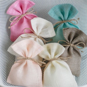 May include: A white wire basket filled with six small burlap gift bags. The bags are tied with twine and come in a variety of colors, including pink, beige, light blue, and brown.