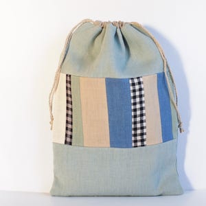 May include: A light blue drawstring bag with a patchwork design of beige, green, blue, and black stripes and checkered fabric.