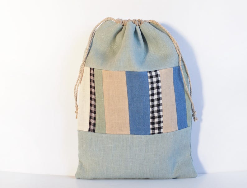 May include: A light blue drawstring bag with a patchwork design of beige, green, blue, and black stripes and checkered fabric.