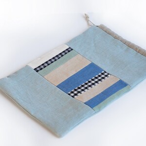 May include: A light blue drawstring bag made of patchwork fabric with stripes and checkered patterns in shades of blue, green, and beige.