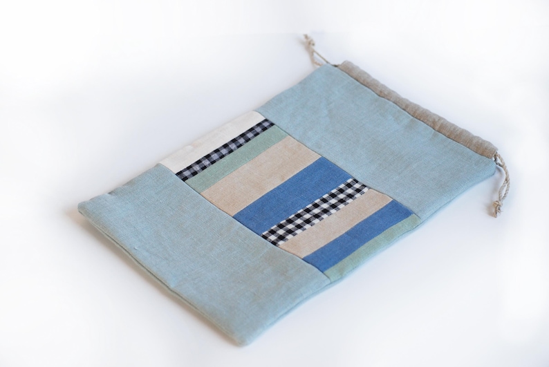 May include: A light blue drawstring bag made of patchwork fabric with stripes and checkered patterns in shades of blue, green, and beige.