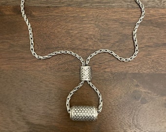 May include: A silver chain necklace with a textured cylindrical pendant. The chain is braided and has a magnetic clasp.