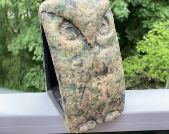 May include: A green and brown ceramic owl sculpture with a hollowed-out back. The owl has a detailed face with large eyes and a beak.