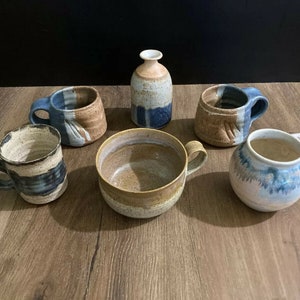 May include: Six ceramic mugs in various shades of blue, brown, and white. The mugs have a rustic, handmade look and are perfect for serving coffee, tea, or other beverages.