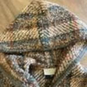 May include: A hooded jacket featuring a thick, textured knit fabric with a multi-colored plaid pattern in shades of brown, tan, grey, and rust. The garment includes a hood, a front opening, and a small rectangular label sewn inside the neckline.