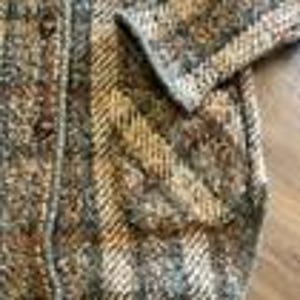 May include: A long-sleeved cardigan featuring a textured knit pattern in shades of brown, tan, gray, and cream. The garment includes a vertical striped design, a button-down front closure with visible buttons, and a patch pocket on the front side.