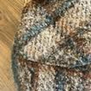 May include: A chunky knit textile featuring a variegated color palette of brown, tan, cream, and slate blue yarns. The fabric displays a thick, textured weave with visible loops and twisted fibers, creating a dense and multi-tonal appearance throughout.