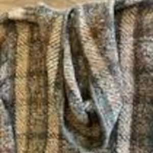 May include: A knit garment featuring a vertical striped pattern in shades of brown, tan, gray, and cream. The fabric has a textured, multi-colored appearance with a visible weave, showcasing a folded section that reveals the interior construction.