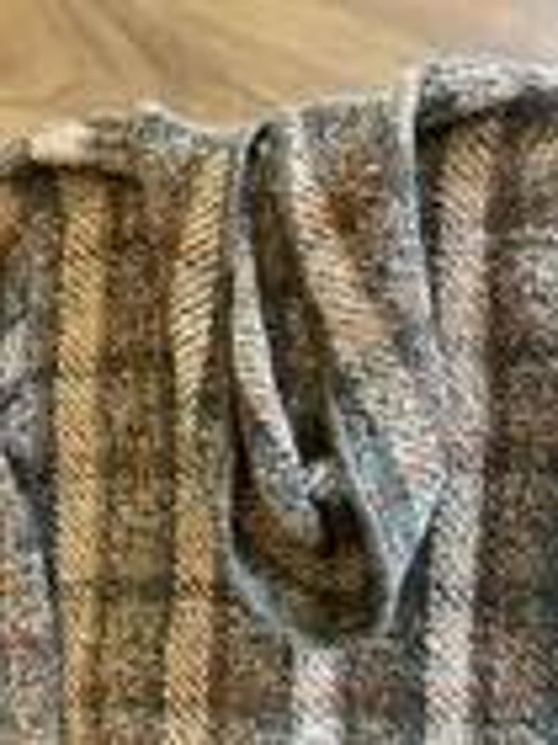 May include: A knit garment featuring a vertical striped pattern in shades of brown, tan, gray, and cream. The fabric has a textured, multi-colored appearance with a visible weave, showcasing a folded section that reveals the interior construction.