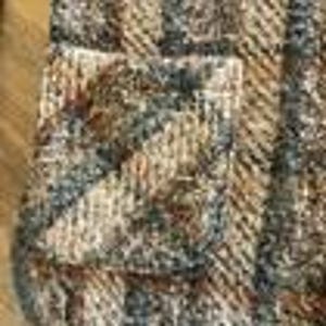 May include: A textured knit fabric featuring a vertical striped pattern in shades of brown, tan, gray, and white. The material displays a thick, woven construction with a visible pocket integrated into the striped design, creating a multi-dimensional surface.