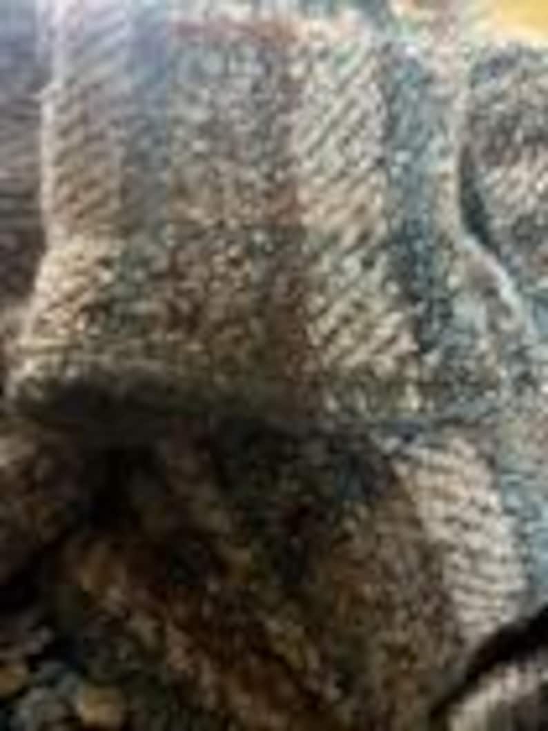 May include: A thick, textured fabric featuring a prominent herringbone weave pattern in shades of charcoal gray, slate blue, and earthy brown. The material displays a dense, multi-tonal appearance with visible interlacing fibers throughout the surface.