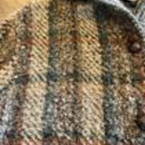 May include: A textured jacket featuring a multi-colored plaid pattern in shades of brown, tan, grey, and black. The garment includes a hood, a front button closure with dark circular buttons, and a thick, woven fabric construction with visible yarn.