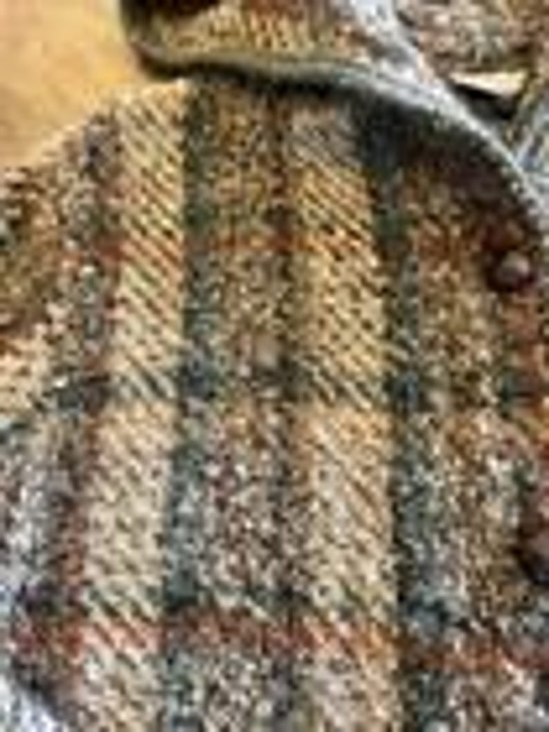 May include: A textured jacket featuring a multi-colored plaid pattern in shades of brown, tan, grey, and black. The garment includes a hood, a front button closure with dark circular buttons, and a thick, woven fabric construction with visible yarn.