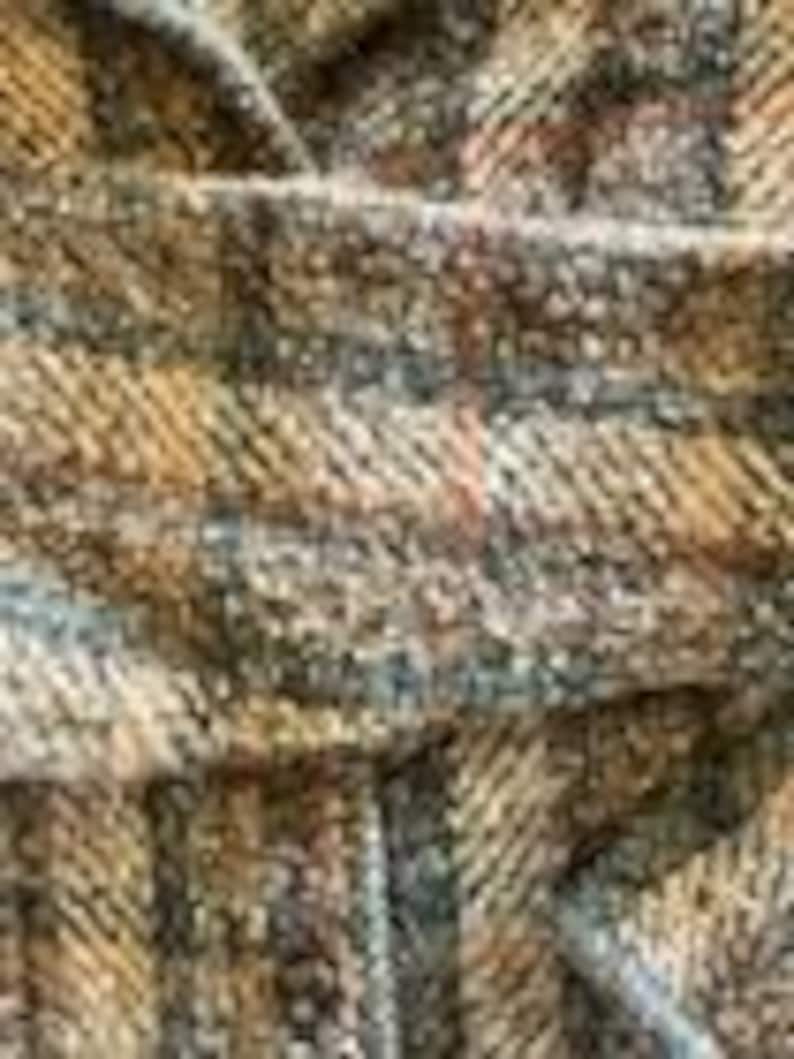 May include: A close-up view of a woven fabric featuring a textured herringbone pattern in shades of brown, tan, and charcoal gray. The material displays a dense, interlaced weave with visible fibers and a multi-tonal appearance throughout the surface.