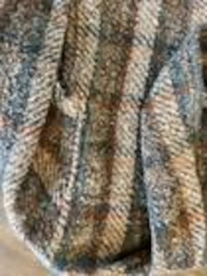 May include: A close-up view of a woven fabric featuring a textured pattern of vertical stripes in shades of brown, tan, gray, and cream. The material displays a distinct diagonal twill weave with visible fibers and a multi-colored, speckled appearance.