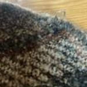 May include: A close-up view of a thick, textured knit fabric featuring a variegated color palette of charcoal gray, deep navy blue, and soft cream tones. The material displays a dense, looped yarn construction with a fuzzy, multi-dimensional surface.