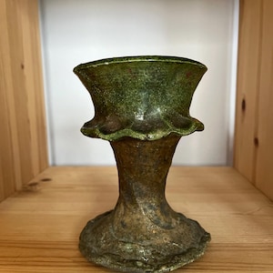 May include: A green ceramic vase with a ruffled rim and a flared base. The vase has a rustic, hand-crafted look.