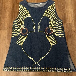 May include: A sleeveless denim dress featuring a yellow graphic of two facing profiles with large hoop earrings. The dress has a decorative hemline and side slits. The design is printed on a dark blue denim fabric.