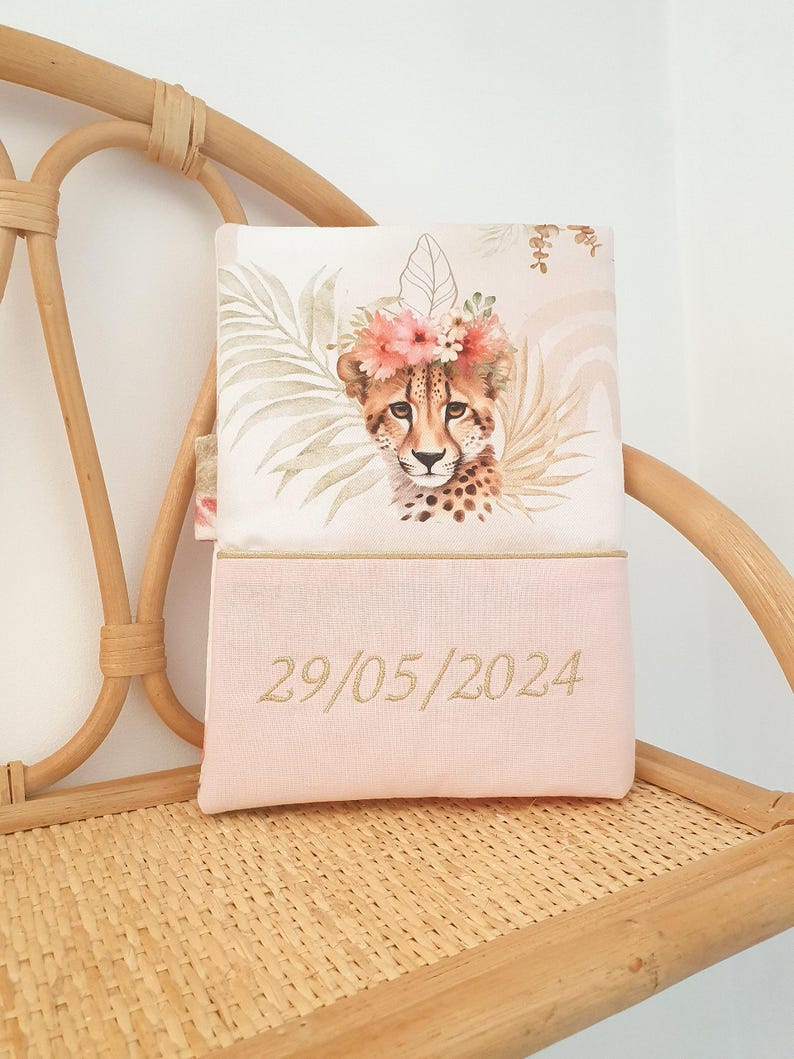 May include: A pink and white pillow with a cheetah wearing a flower crown and a date embroidered on the bottom. The date is 29/05/2024.
