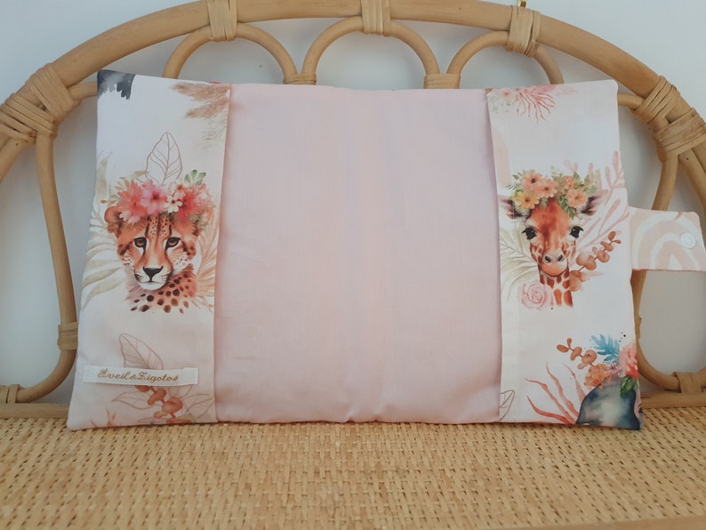 May include: A pink pillow with a cheetah and giraffe print on the front and back. The pillow has a floral design and the text "Eveil & Sigolo" on the front.