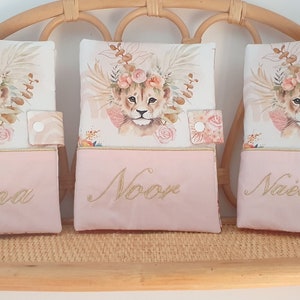 May include: Three pink and white fabric pouches with a lion cub design and embroidered names: Eliana, Noor, and Naelany.