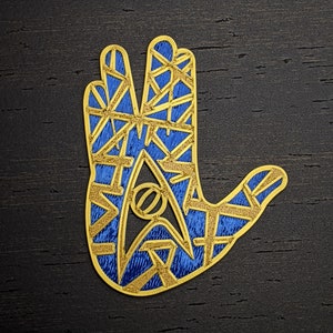 May include: A gold and blue embroidered hand with a stylized star trek symbol in the center.