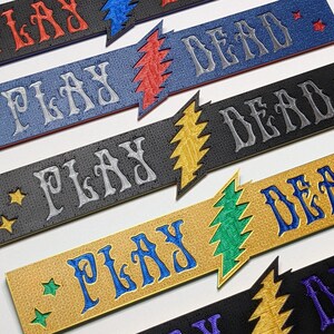 May include: Five embroidered patches with the text "Play Dead" in different colors and fonts. The patches feature a lightning bolt design with a stylized tree inside.