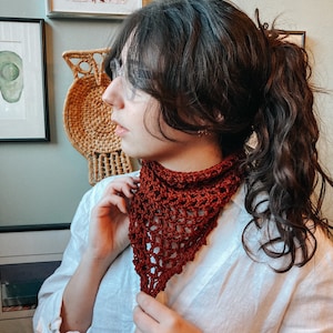 May include: A woman wearing a white shirt with a rust-colored crocheted scarf around her neck. The scarf is a triangular shape with a lacy pattern.