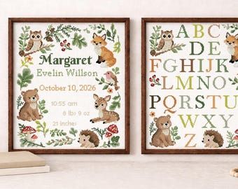 May include: Two framed cross-stitch artworks. One features a personalized birth announcement with a bear, deer, fox, owl, and hedgehog. The other displays the alphabet with similar woodland creatures. The frames are brown.