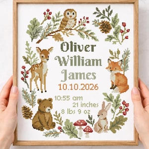 May include: A framed cross-stitch pattern featuring a woodland theme with an owl, deer, fox, bear, and rabbit surrounded by foliage. The text reads Oliver William James, 10.10.2026, 10:55 am, 21 inches, and 8 lbs 9 oz in a decorative font.