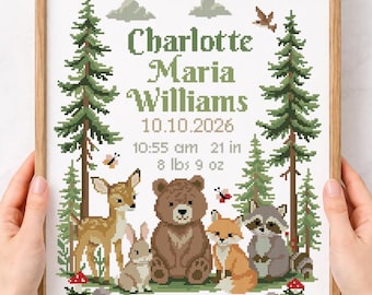 May include: A framed cross-stitch pattern featuring the name Charlotte Maria Williams, the date 10.10.2026, 10:55 am, 21 in, and 8 lbs 9 oz. The design includes green pine trees, a deer, a rabbit, a bear, a fox, a raccoon, butterflies, and mushrooms.