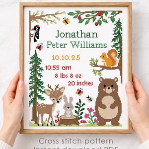 Könnte beinhalten: Ein gerahmtes Kreuzstichmuster mit Waldthema, das ein Reh, ein Kaninchen, einen Bären und ein Eichhörnchen zeigt. Das Design enthält den Namen "Jonathan Peter Williams" und Geburtsdetails. Der Rahmen wird von Händen gehalten. Der Text "Cross stitch pattern Instant download PDF" steht unten.