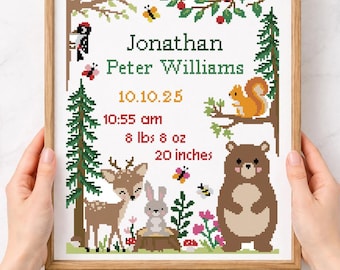 May include: A framed cross-stitch pattern featuring a woodland theme. The design includes a deer, rabbit, bear, and squirrel, with the name "Jonathan Peter Williams" and birth details. The frame is held by hands. The text "Cross stitch pattern Instant download PDF" is at the bottom.