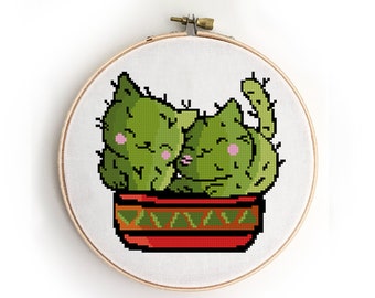 May include: Two green cactus cats in a red and green pot. The cats are hugging and have pink cheeks.