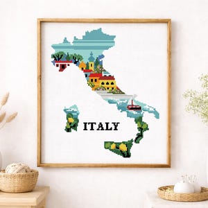 Könnte beinhalten: Gerahmtes Kreuzstich-Kunstwerk, das die Karte von Italien darstellt. Die Karte ist mit farbenfrohen, pixeligen Bildern von Gebäuden, Wasser und Grün gefüllt. Das Wort "ITALY" ist in Schwarz gestickt. Das Kunstwerk wird an einer weißen Wand ausgestellt.