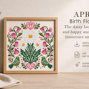 May include: A framed cross-stitch design featuring a floral pattern with pink flowers, green leaves, and two green birds. The text "APRIL Birth Flowers" is displayed above the design. The daisy looks simple and happy and stands for innocence and purity.